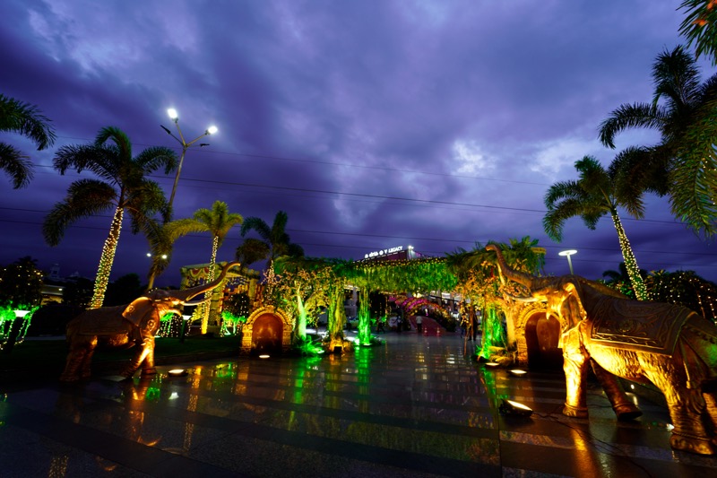 Illuminated garden with elephant sculptures and palms at night